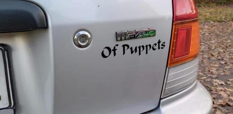 Ein Auto, auf der Heckklappe steht das Typenschild „Mazda“ und darunter „of Puppets“