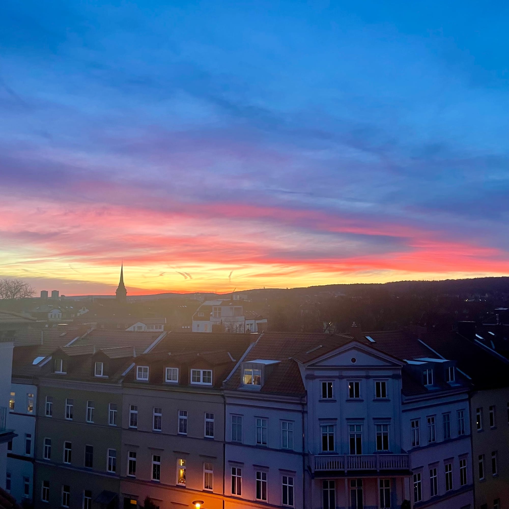 Sonnenaufgang über der Stadt, Häuser leuchten und der Himmel hat viele dunkle, lila Farben.